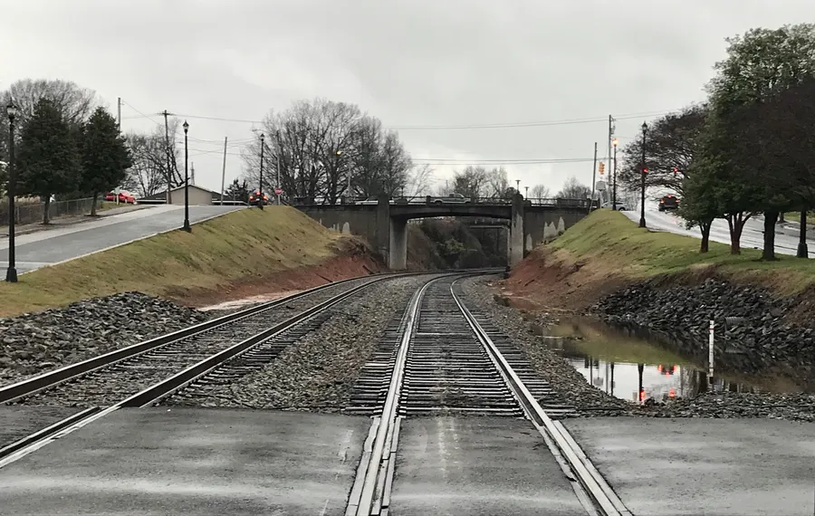 Railroad tracks curving under a concrete road bridge in Kings Mountain, NC, on an overcast day
